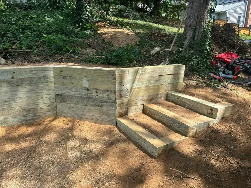 Wooden retaining wall with built-in steps in a wooded backyard.