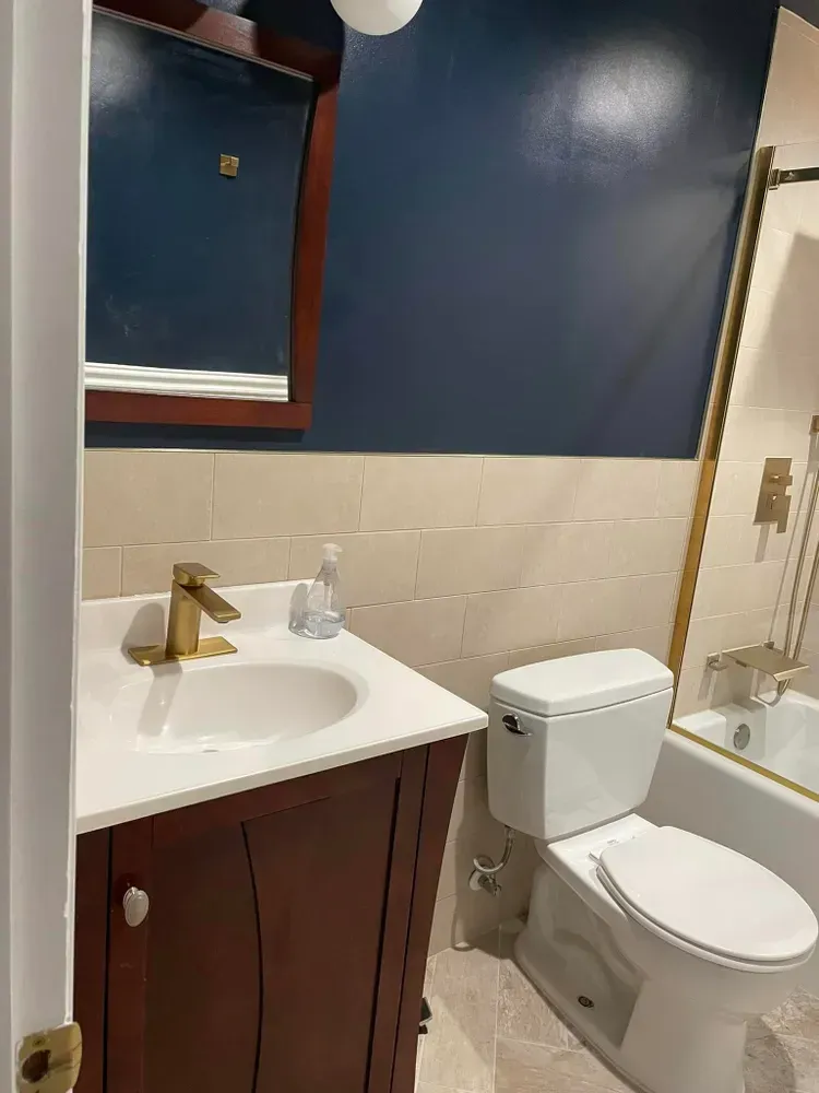 Small bathroom with white sink and toilet, navy walls, beige tile, and a shower curtain edge visible.