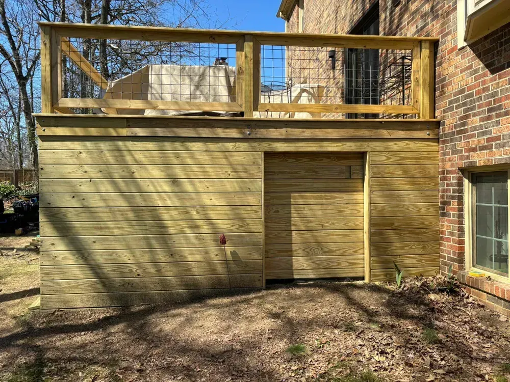 Wooden house extension with a rooftop deck and railing beside a brick building