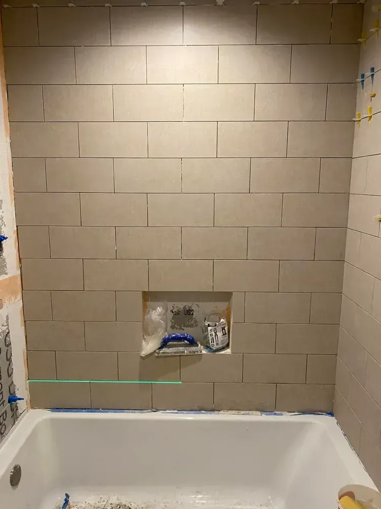 Bathroom tub alcove with beige tiled shower wall and a recessed shelf above the tub.