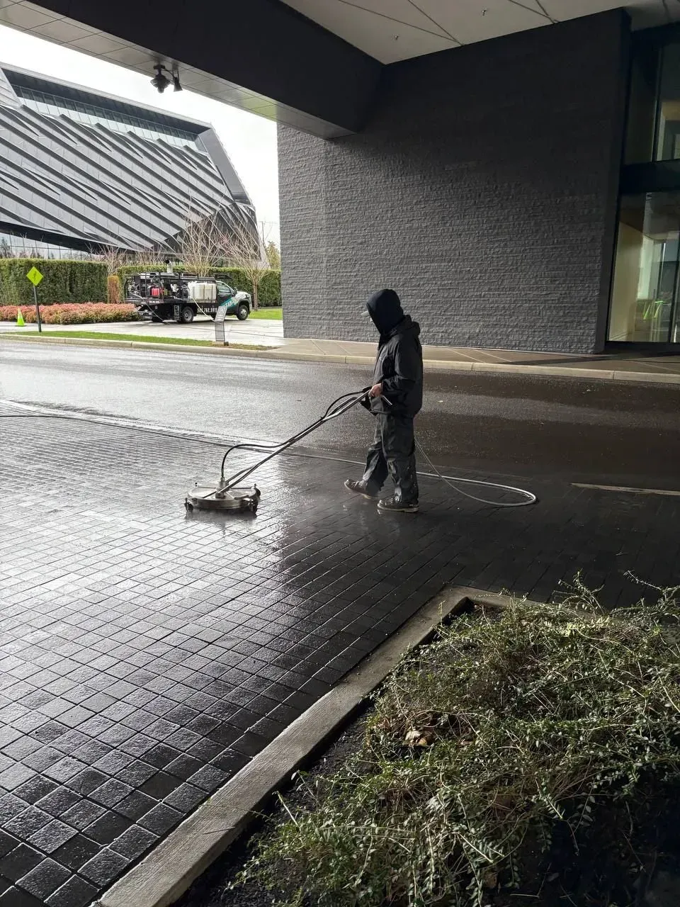 Person pressure washing a brick paved area under an overhang.