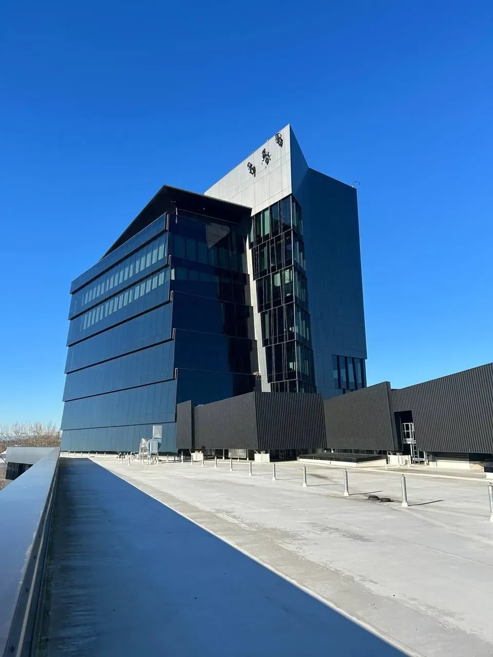 Modern black glass building with angled roof against a clear blue sky.
