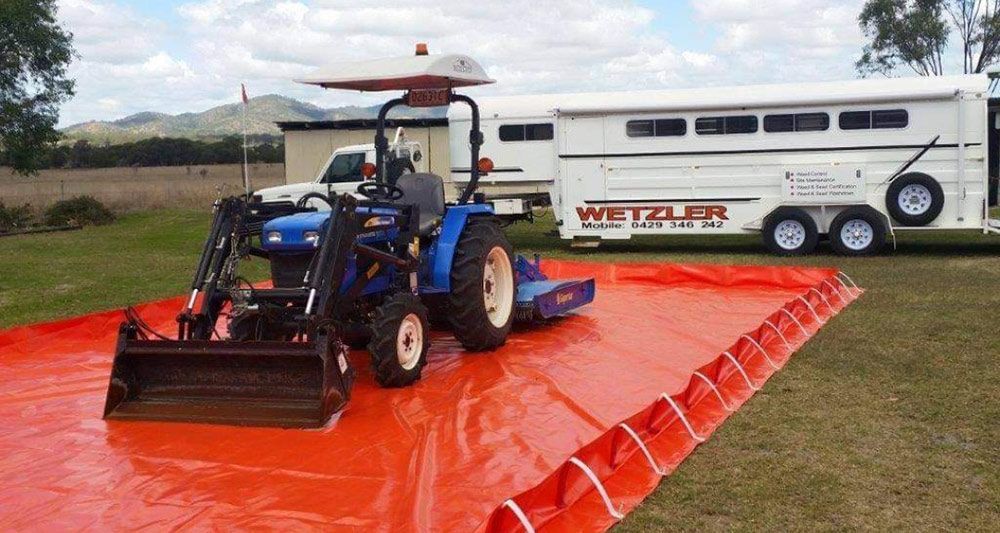 Tractor Is Parked On An Orange Tarp Next To A Trailer — Wetzler Pty Ltd In Marmor QLD