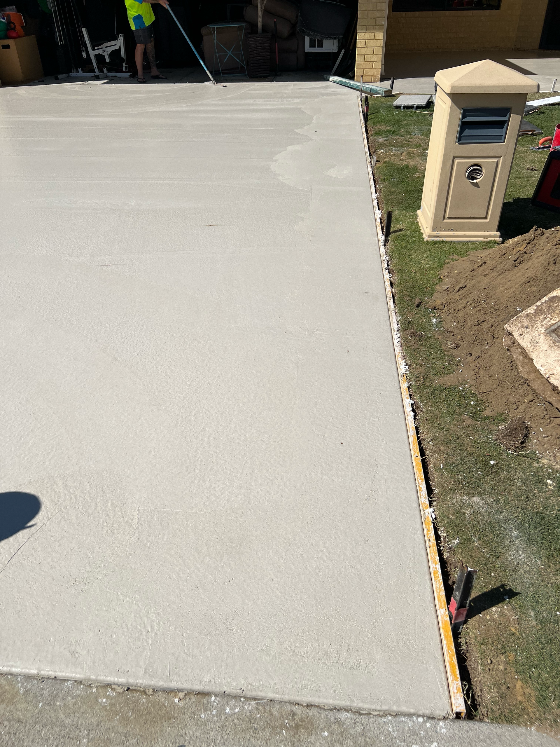 Concrete driveway beside a landscaped lawn, with a stone mailbox pillar on the right.
