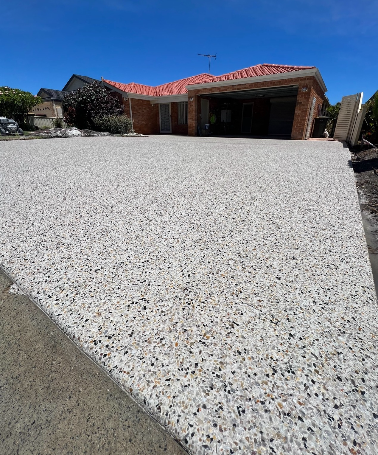 White pebble driveway leading to a red-roofed suburban house under a clear blue sky