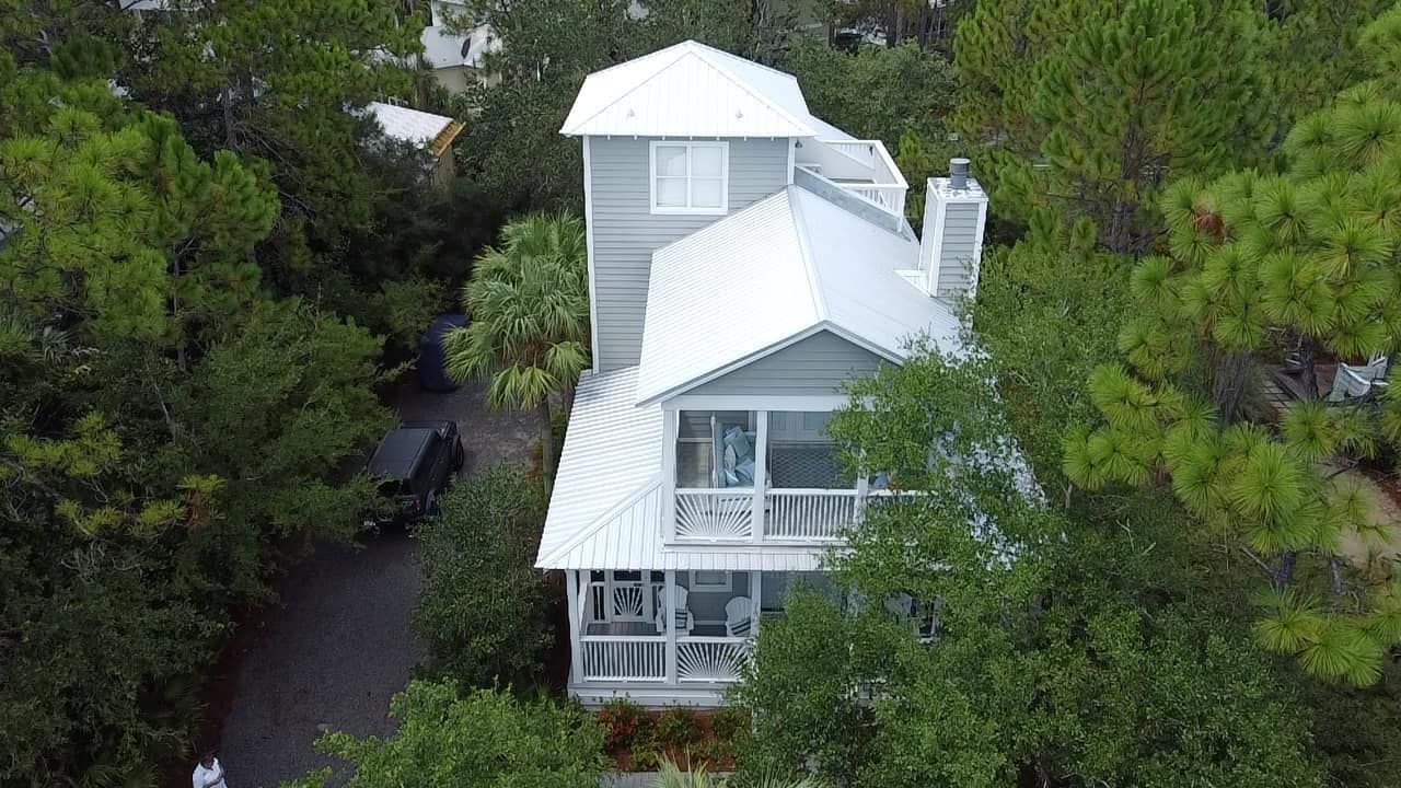 White house with tower and wraparound porch surrounded by dense green trees, viewed from above