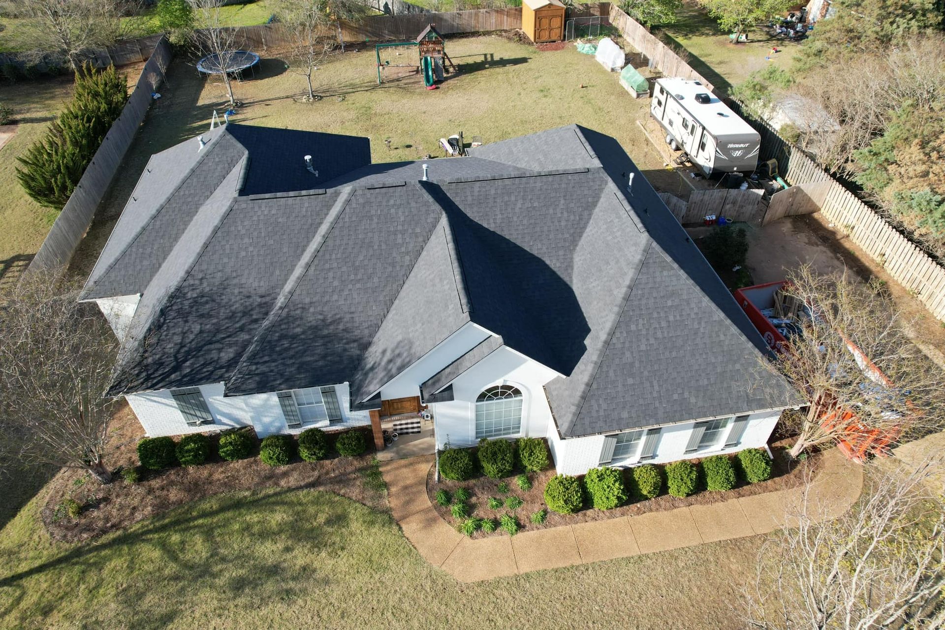 Aerial view of a gray-roofed house with a fenced yard and a white truck parked nearby.
