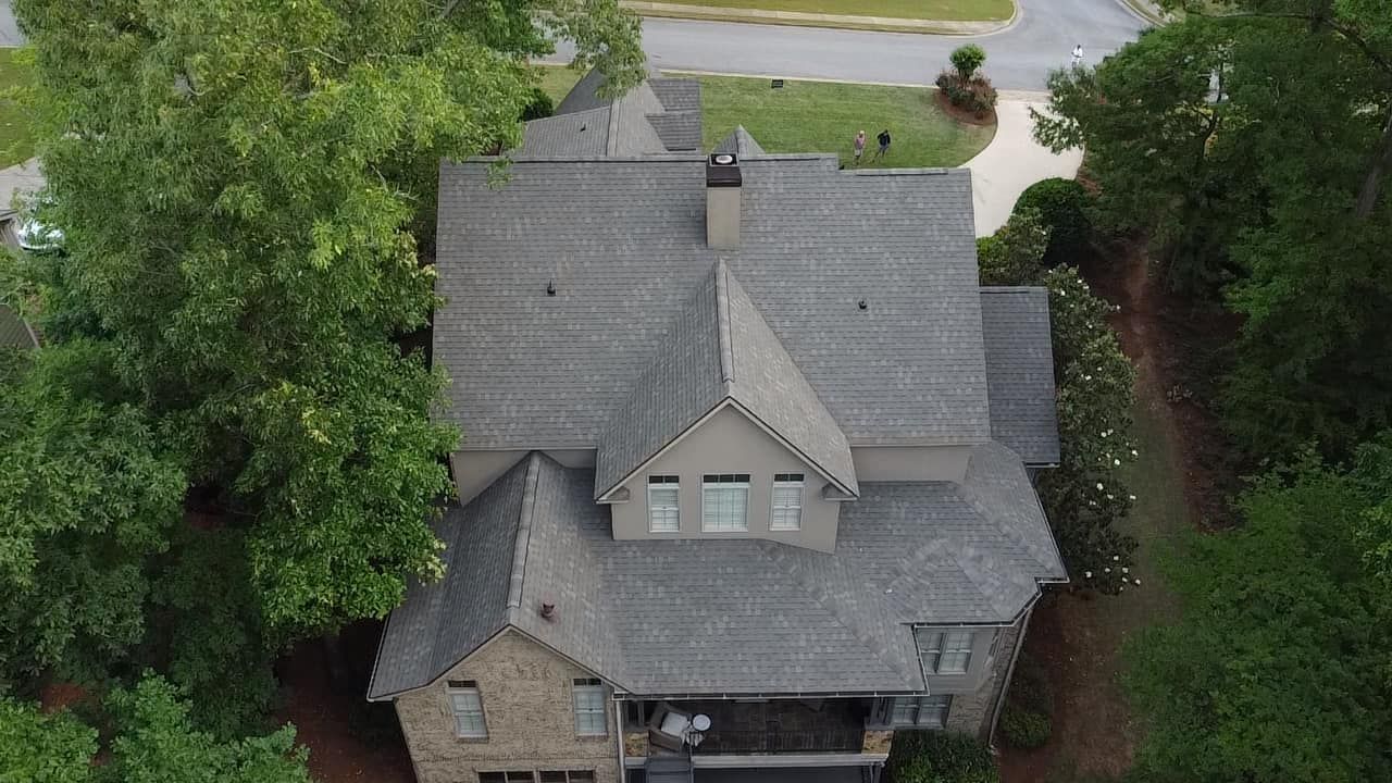 Aerial view of a gray-roofed house surrounded by trees and a driveway.