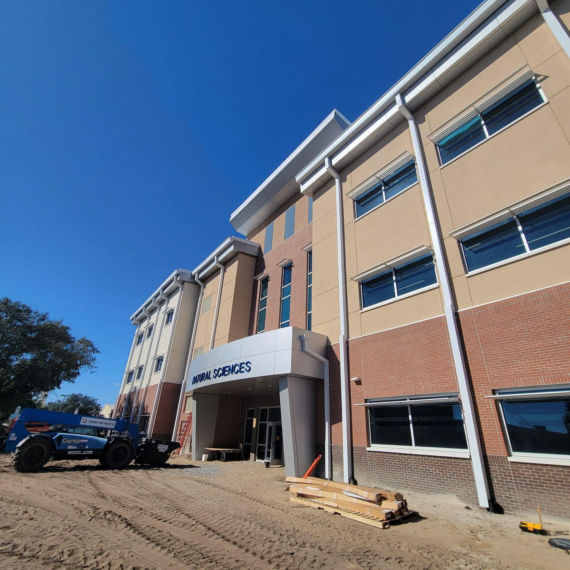 Modern hotel exterior with a driveway, parked vehicle, and clear blue sky