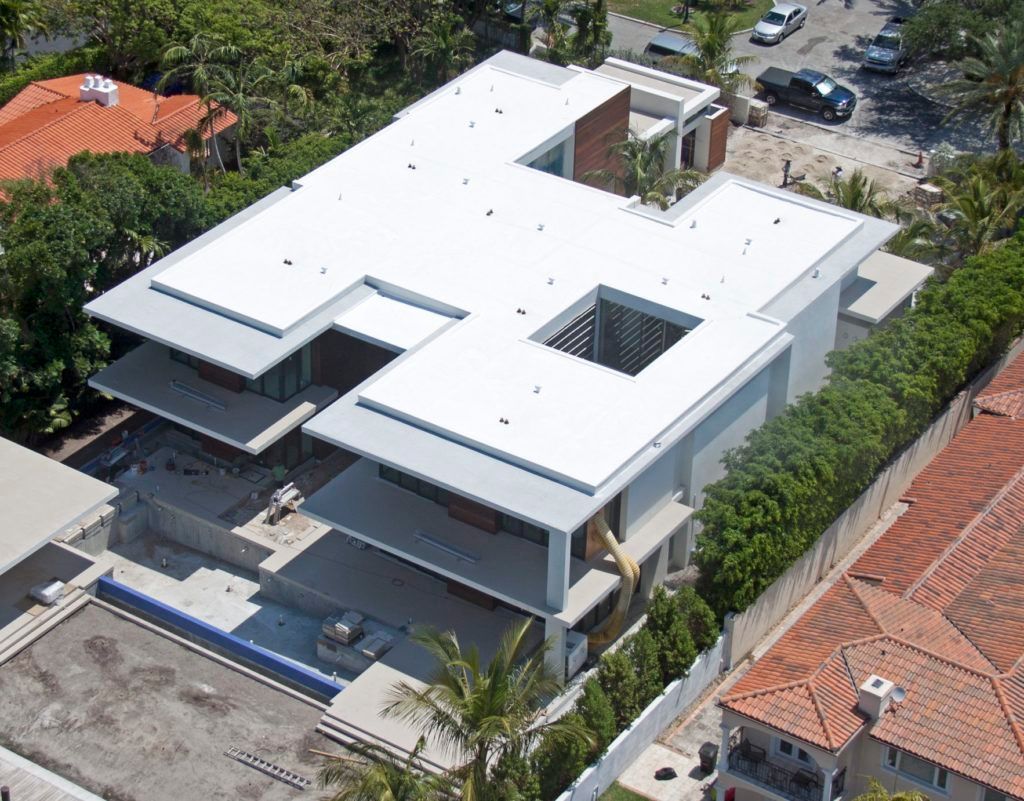 Aerial view of a modern white house with rooftop openings and red-roofed neighboring homes nearby