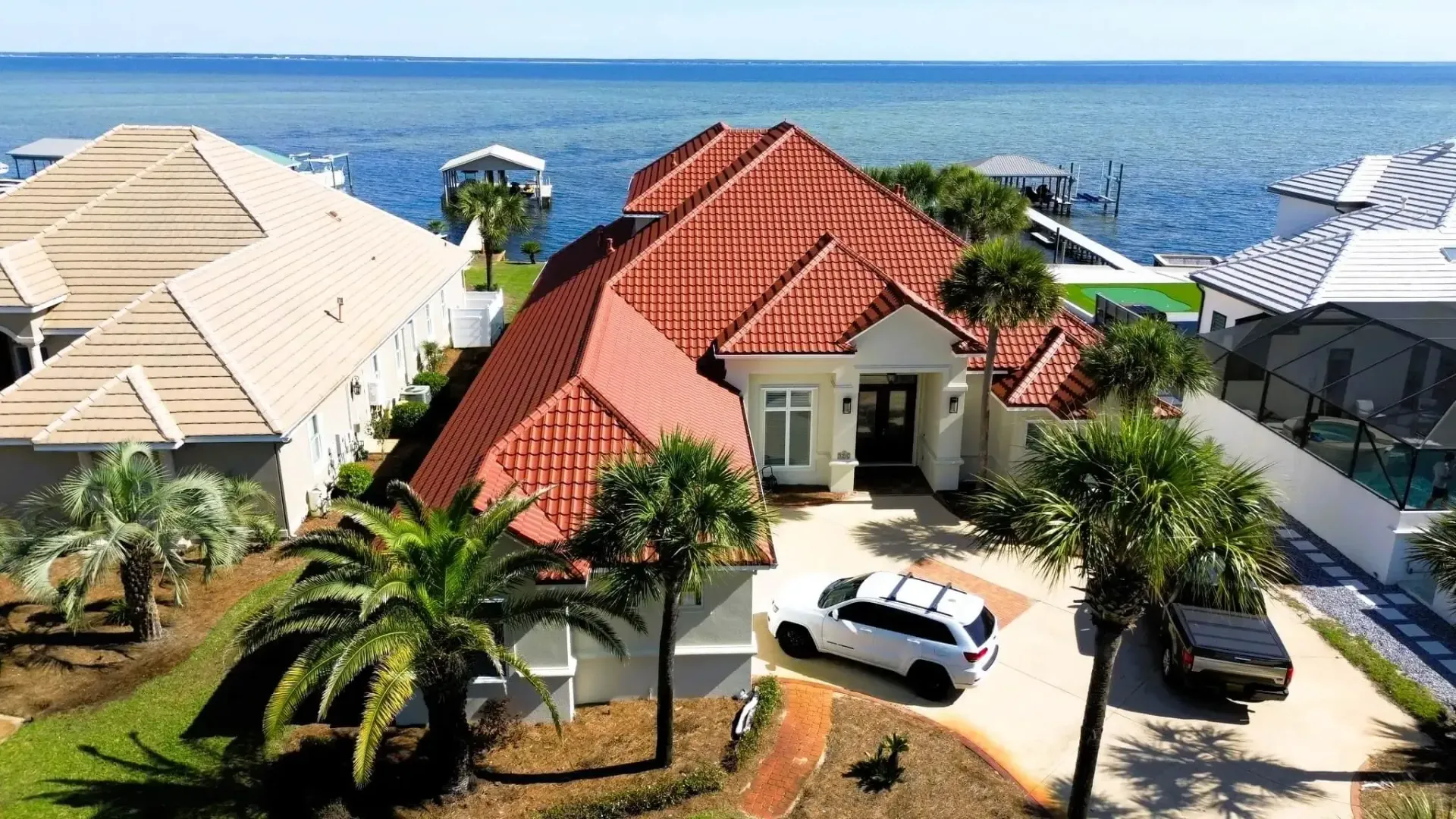 Coastal villa with red roof and parked white car, overlooking the ocean under a clear blue sky