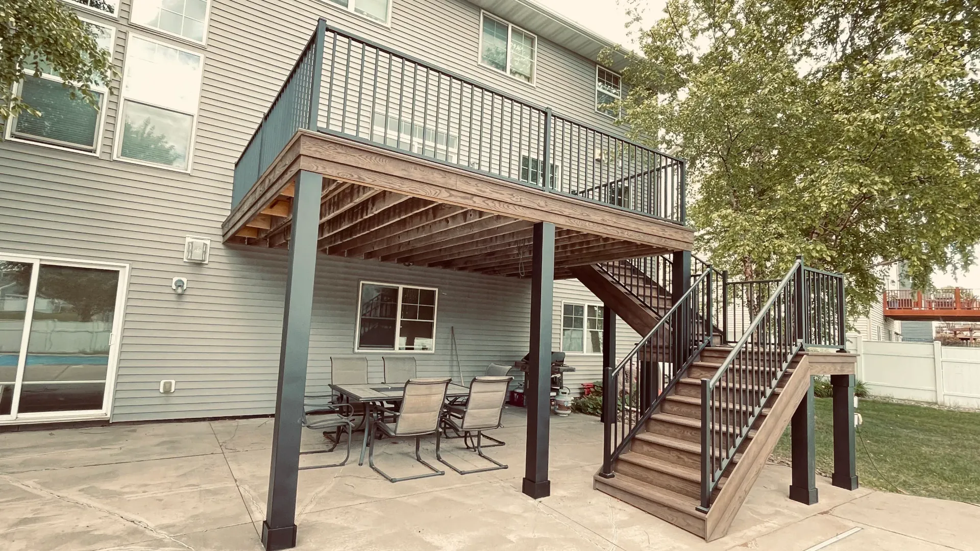 Custom maintenance-free raised deck with wood-look boards, black metal railings, stairs, and a cover