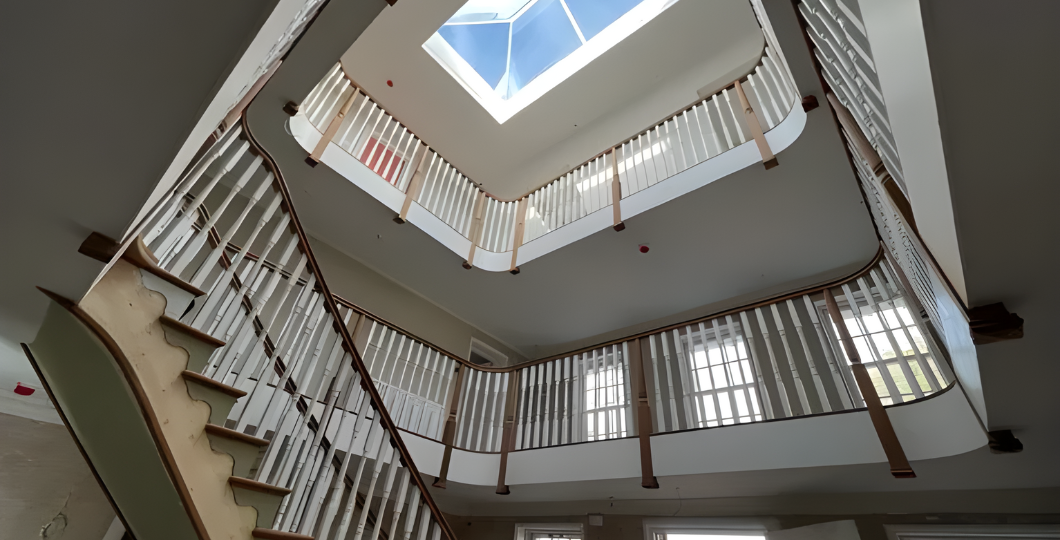 Spiral staircase around a skylit atrium with white railings and beige walls