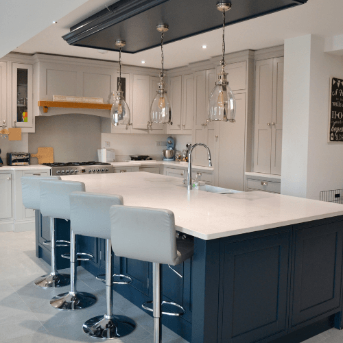Modern white kitchen with navy island, marble counters, pendant lights, and four stools
