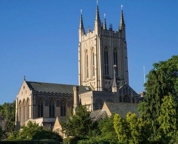 Stone cathedral with a tall tower and pointed spires above trees under a blue sky