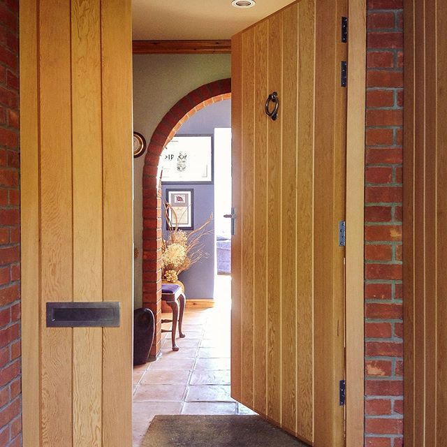 Open wooden front door framing a tiled hallway and sunlit dining room beyond