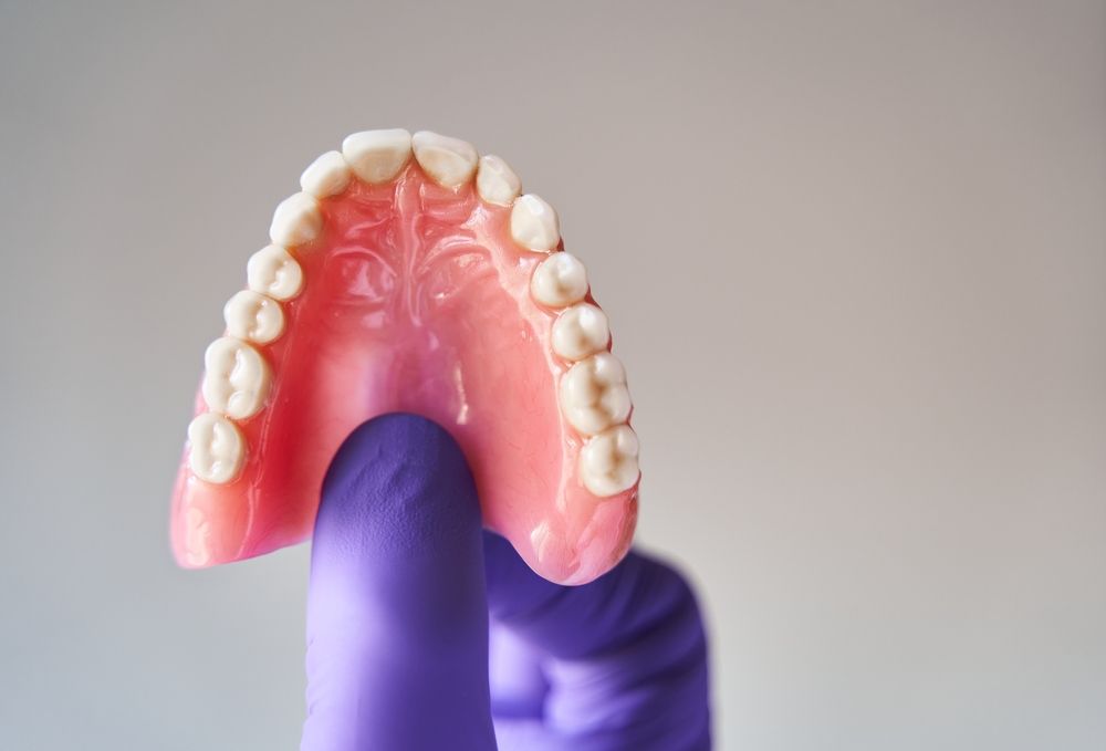 A Person Wearing Purple Gloves is Holding a Denture in Their Hand — The Denture Kitchen in Maroochydore, QLD