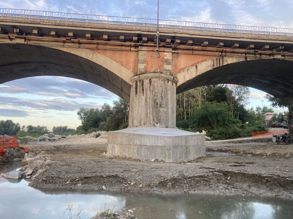 Ponte con sostegni ad arco e pilastro centrale sopra il letto di un fiume in secca. Cielo nuvoloso sullo sfondo.