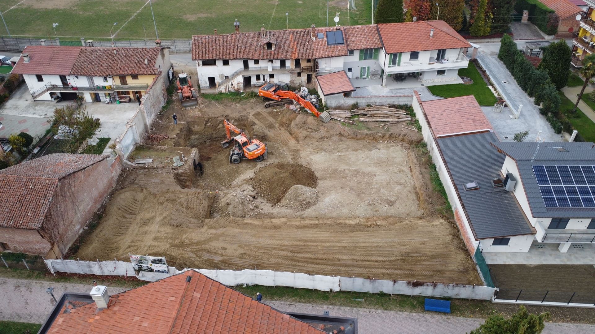 Callimaco - Centallo. Vista aerea di un cantiere con escavatori in azione, circondato da case con tetti in terracotta.