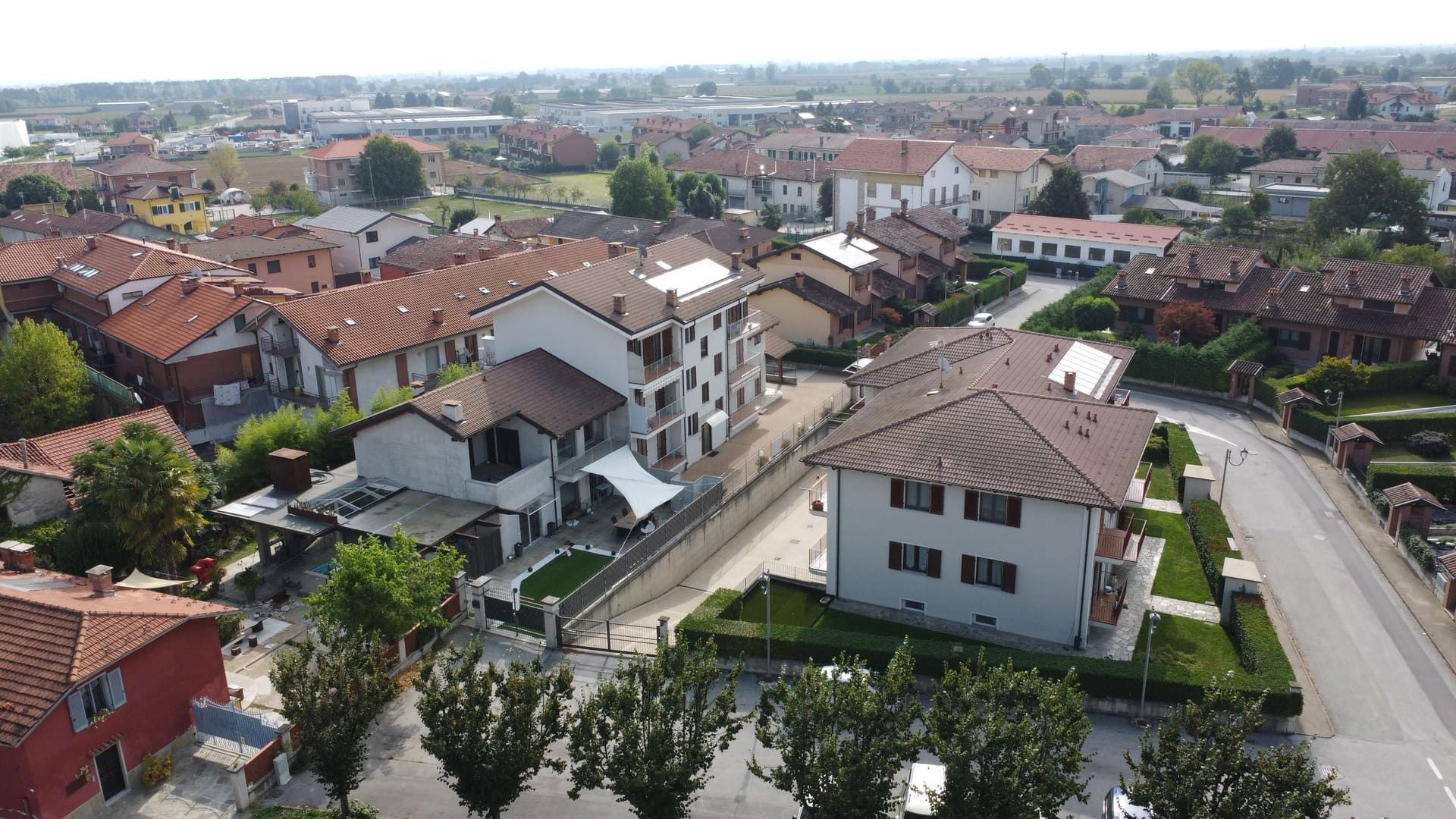 Isotta - Villafalletto. Vista aerea di una città con tetti di tegole rosse, edifici, alberi verdi e una strada.