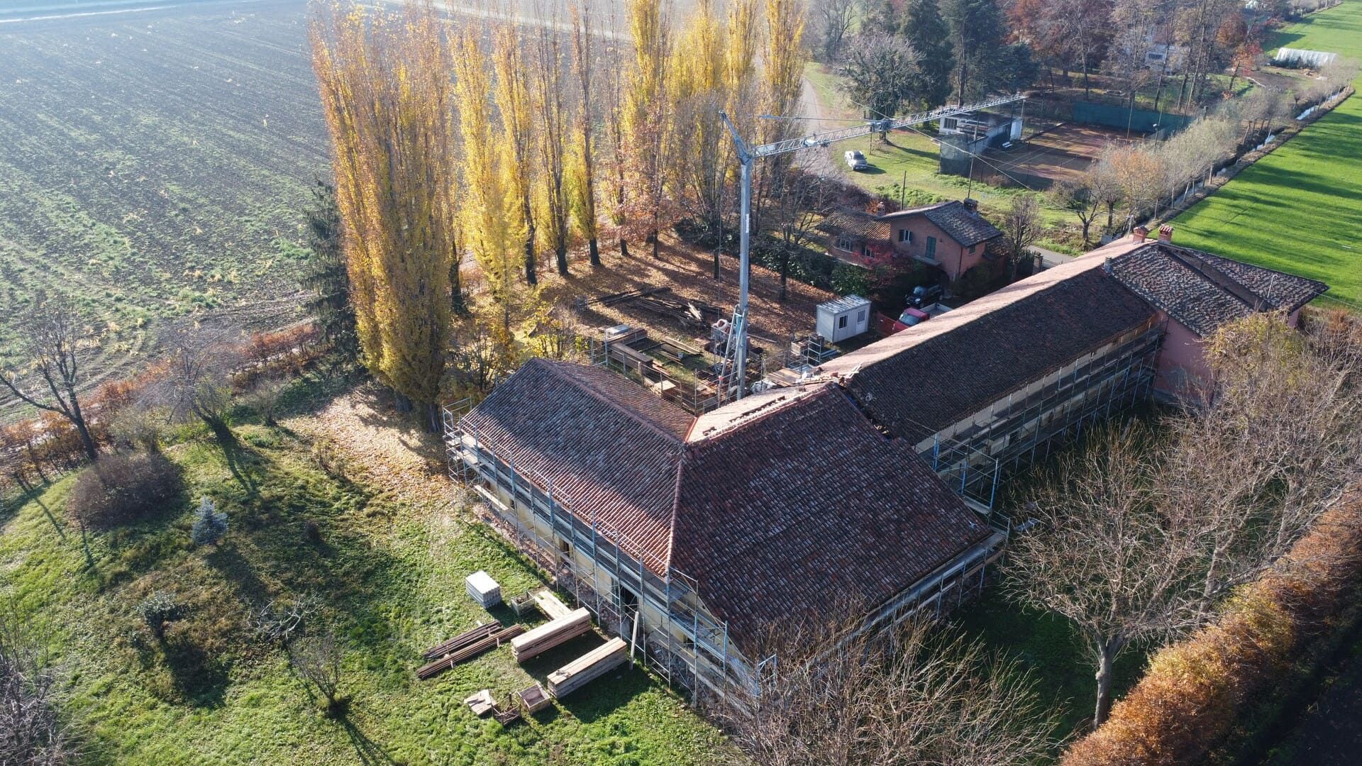Vista aerea di un edificio in mattoni con tetto marrone, ciminiera e alberi in un campo.