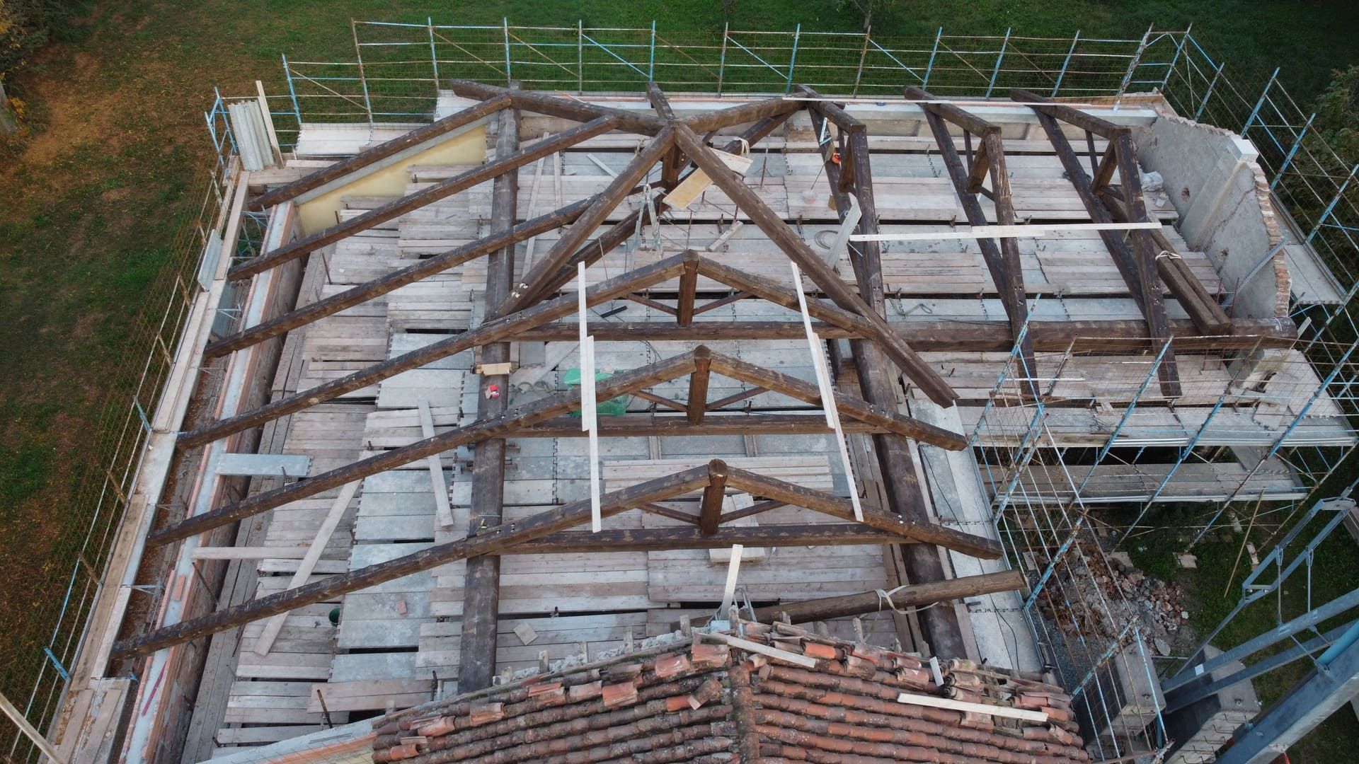 Vista aerea di una struttura del tetto con travi in ​​legno a vista, impalcature e alcune tegole originali.
