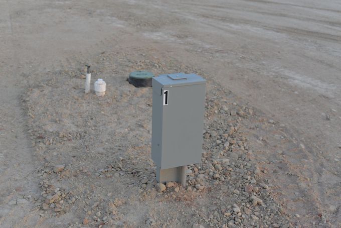 Gray utility box with a blue top on a gravel lot, with small pipes nearby