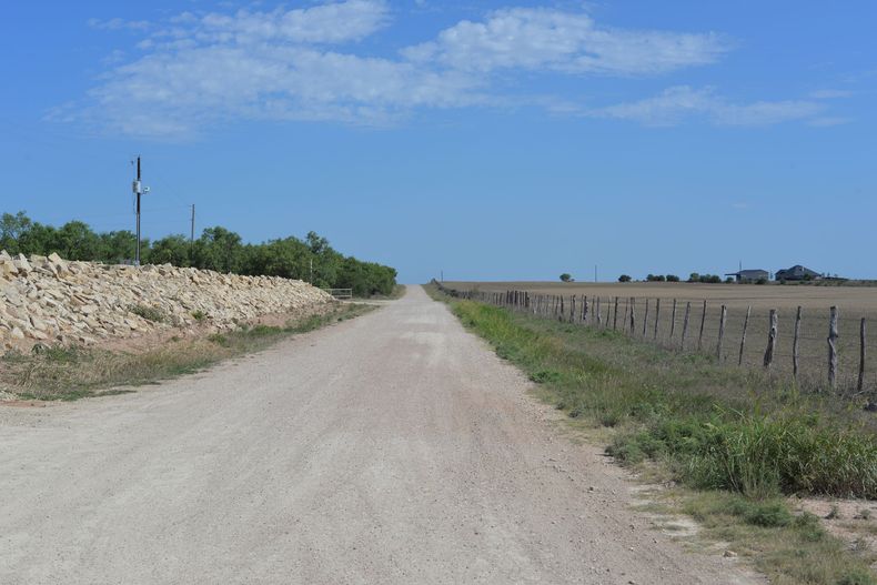 Gravel road stretching through open fields under a blue sky with scattered clouds