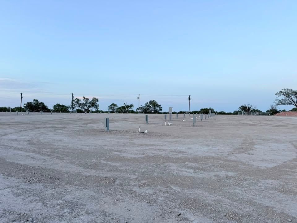 Empty gravel lot under a pale blue sky with utility poles and distant trees