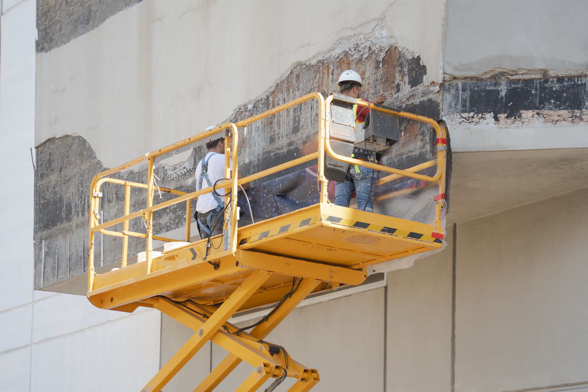 A worker in a yellow high-visibility shirt stands in a construction zone with shored ceiling supports and wall panels.