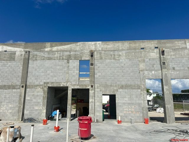 Concrete wall construction site with open doorways and windows under a bright blue sky.