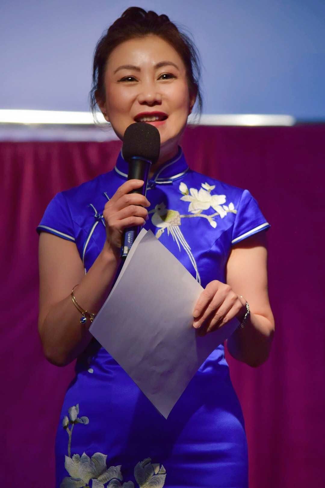 A woman in a blue dress is holding a microphone and a piece of paper