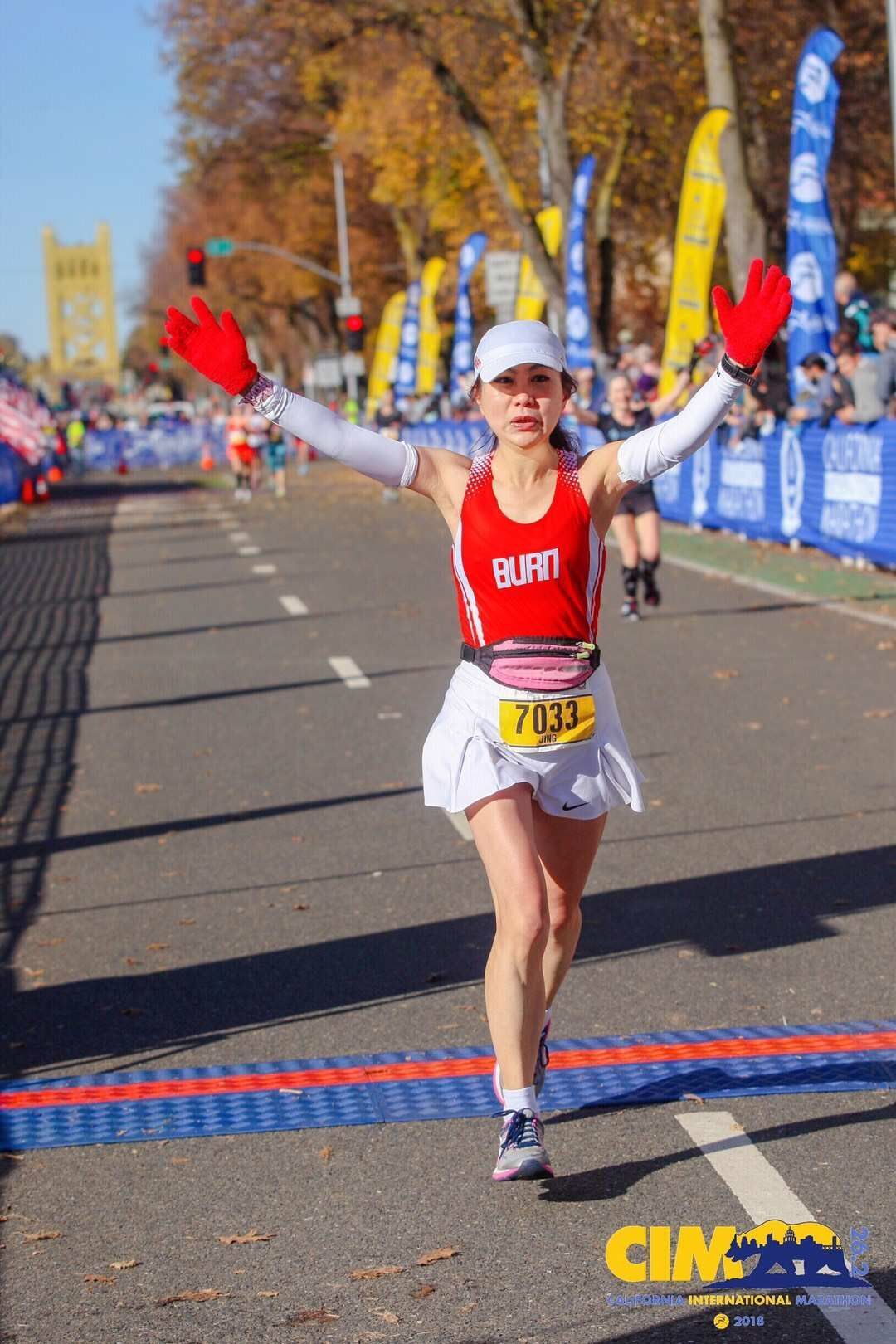 A woman is crossing the finish line of a marathon with her arms outstretched.