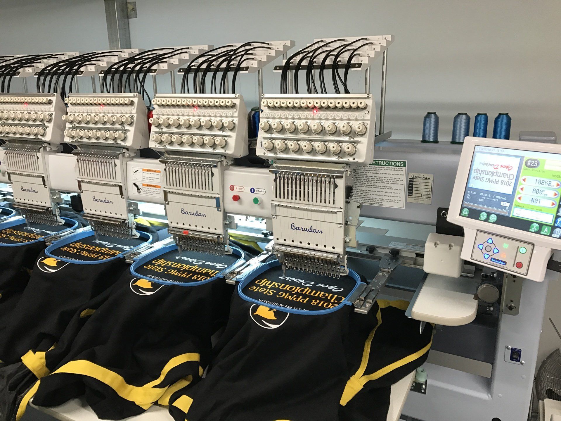 Industrial embroidery machines stitching white fabric pieces in a factory line