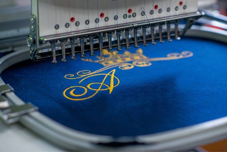 Embroidery machine stitching gold monogram on blue fabric