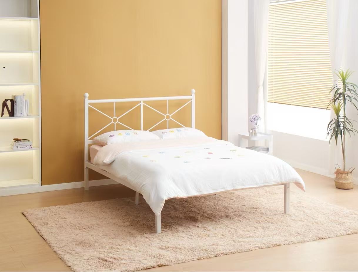 White metal bed frame with white bedding, on a beige rug, in a room with a gold wall.