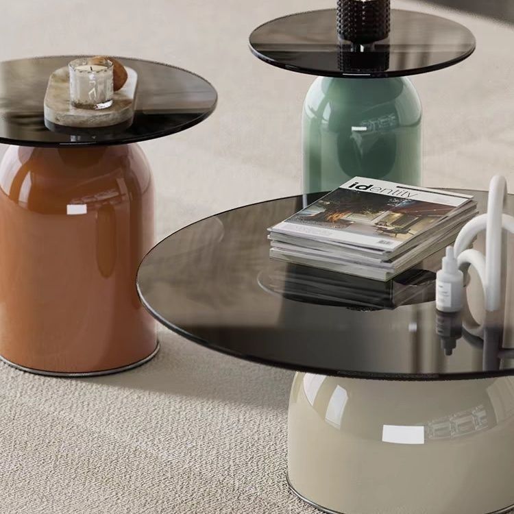 Three modern side tables with dark glass tops, in orange, green, and beige.