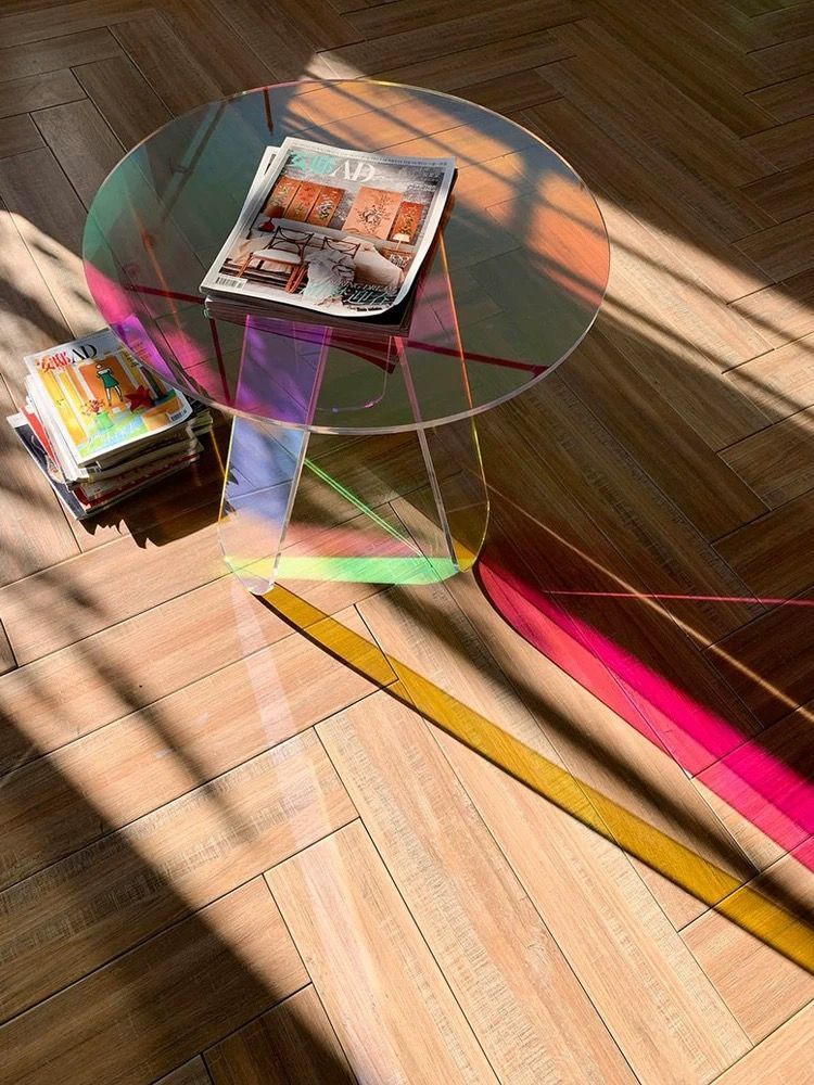Round iridescent coffee table with magazines on a wooden floor, lit by sunlight.
