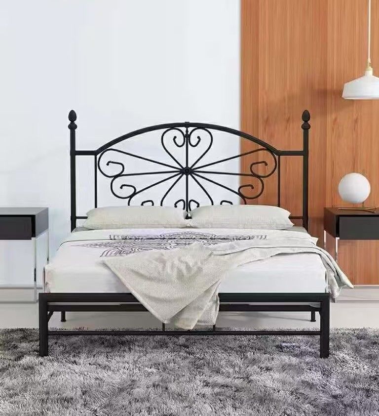 Black metal bed frame with decorative headboard; white bedding, gray rug.