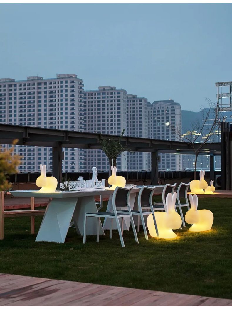 Outdoor dining area with glowing bunny-shaped lights, table, chairs, and city skyline background.