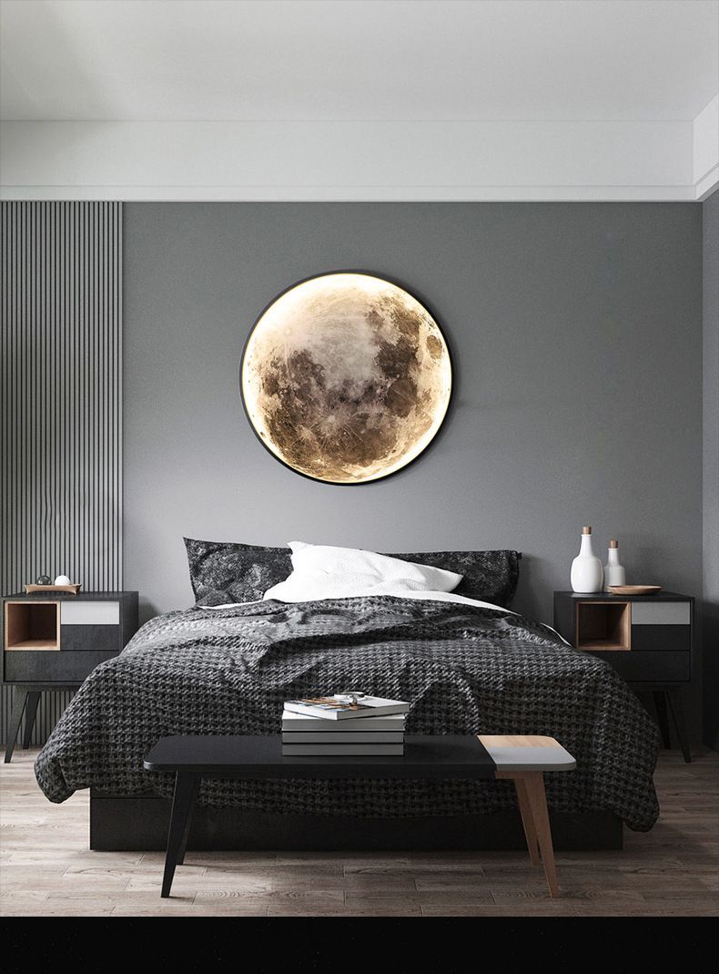 Bedroom with a large moon-shaped light above a bed with dark bedding; nightstands, and a bench. Gray walls.