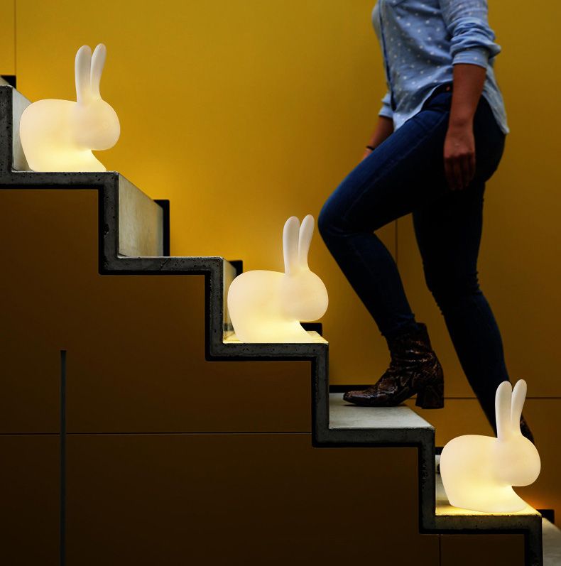 Glowing bunny-shaped lights illuminate steps as a person walks up them, against a yellow wall.
