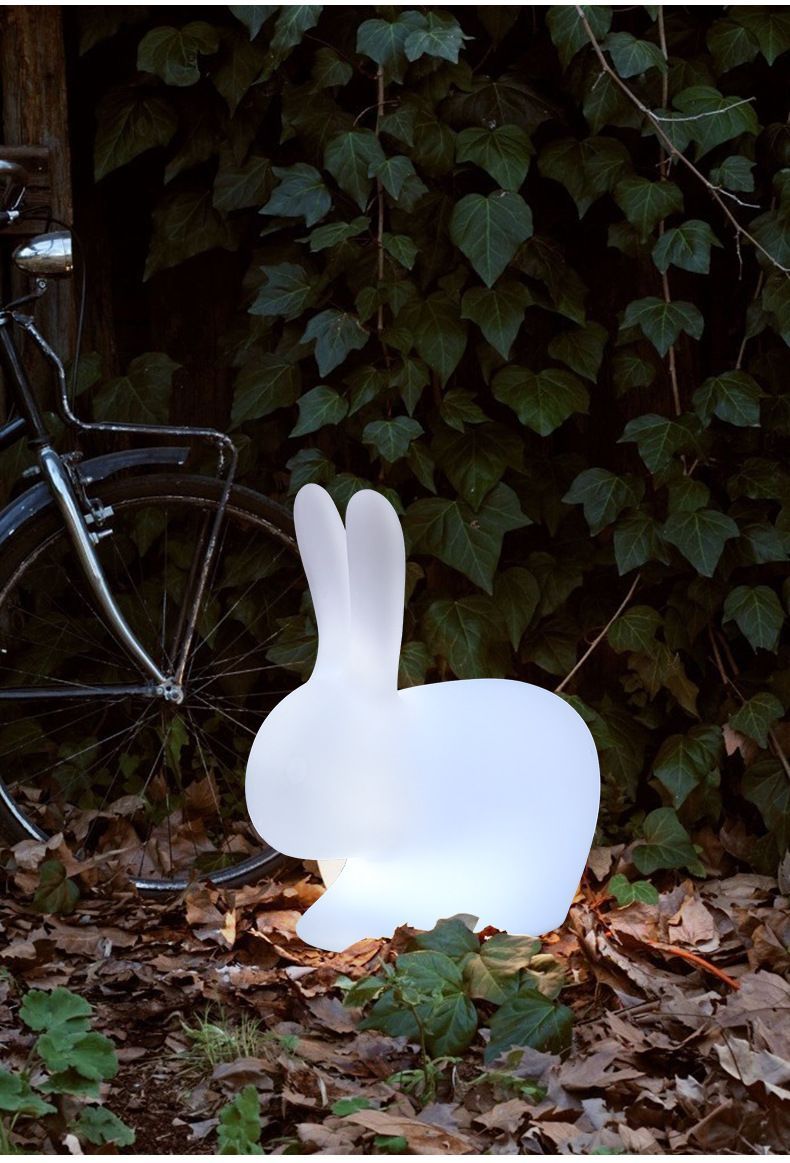 Glowing white rabbit-shaped outdoor lamp, illuminated near ivy and a bicycle.