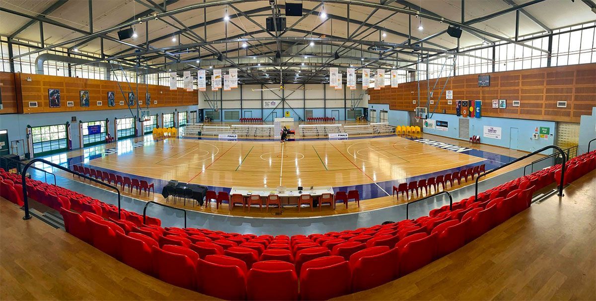 Indoor basketball court with red bleachers and polished wooden floor in a gymnasium.
