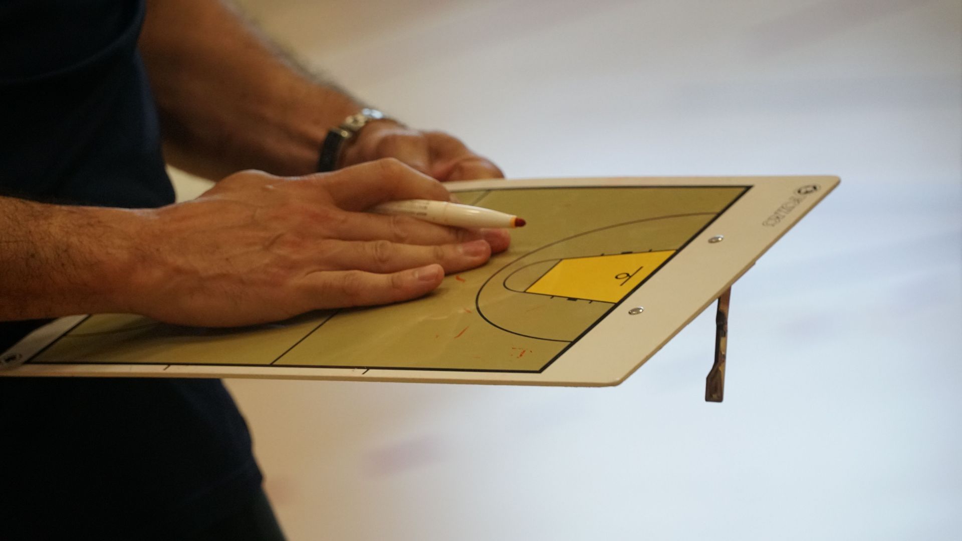 Hands sketching a cardboard model with a pencil on a table, showing a yellow cutout section