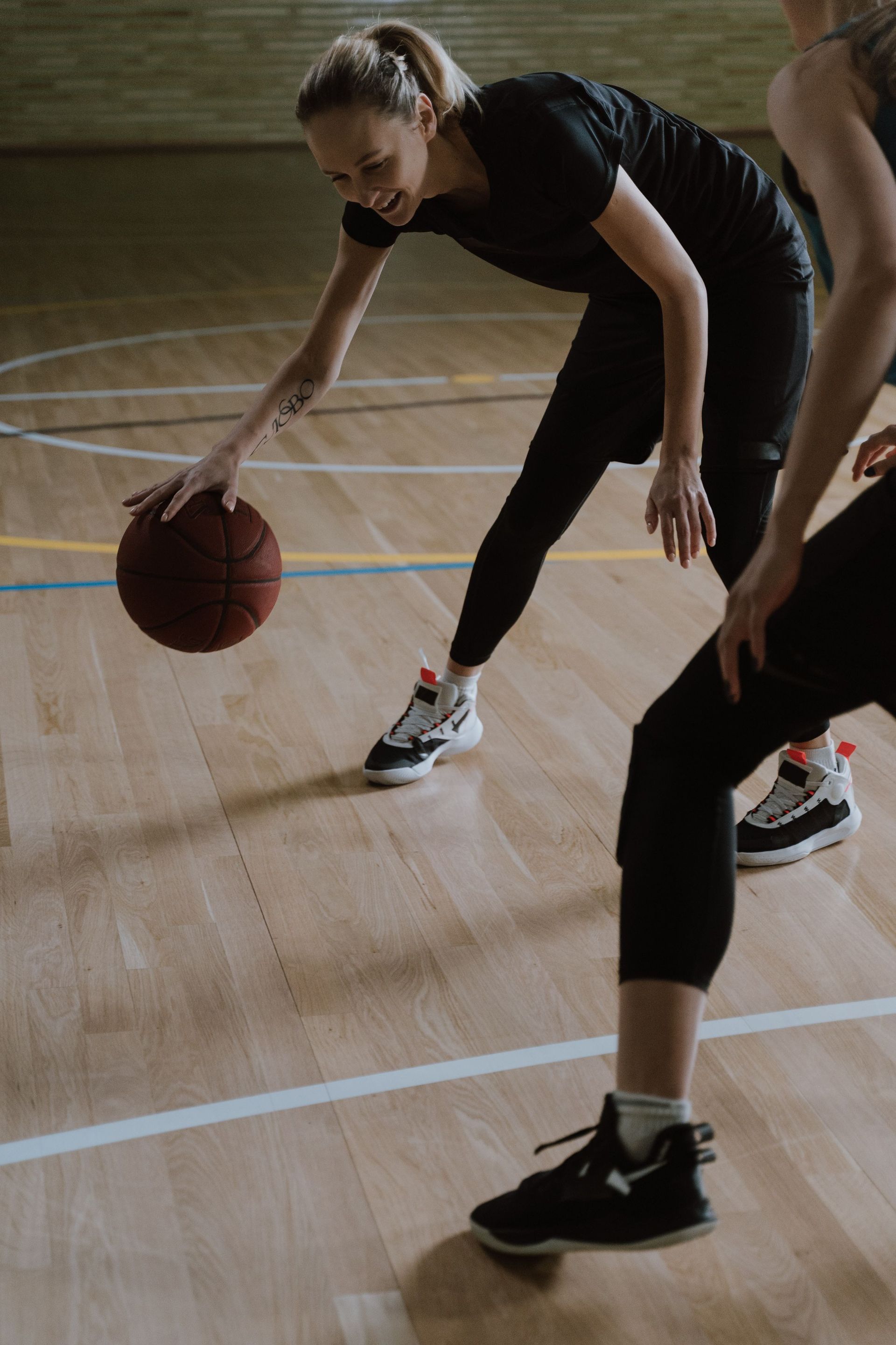 Basketball player dribbling on an indoor court, bent low in a defensive stance.