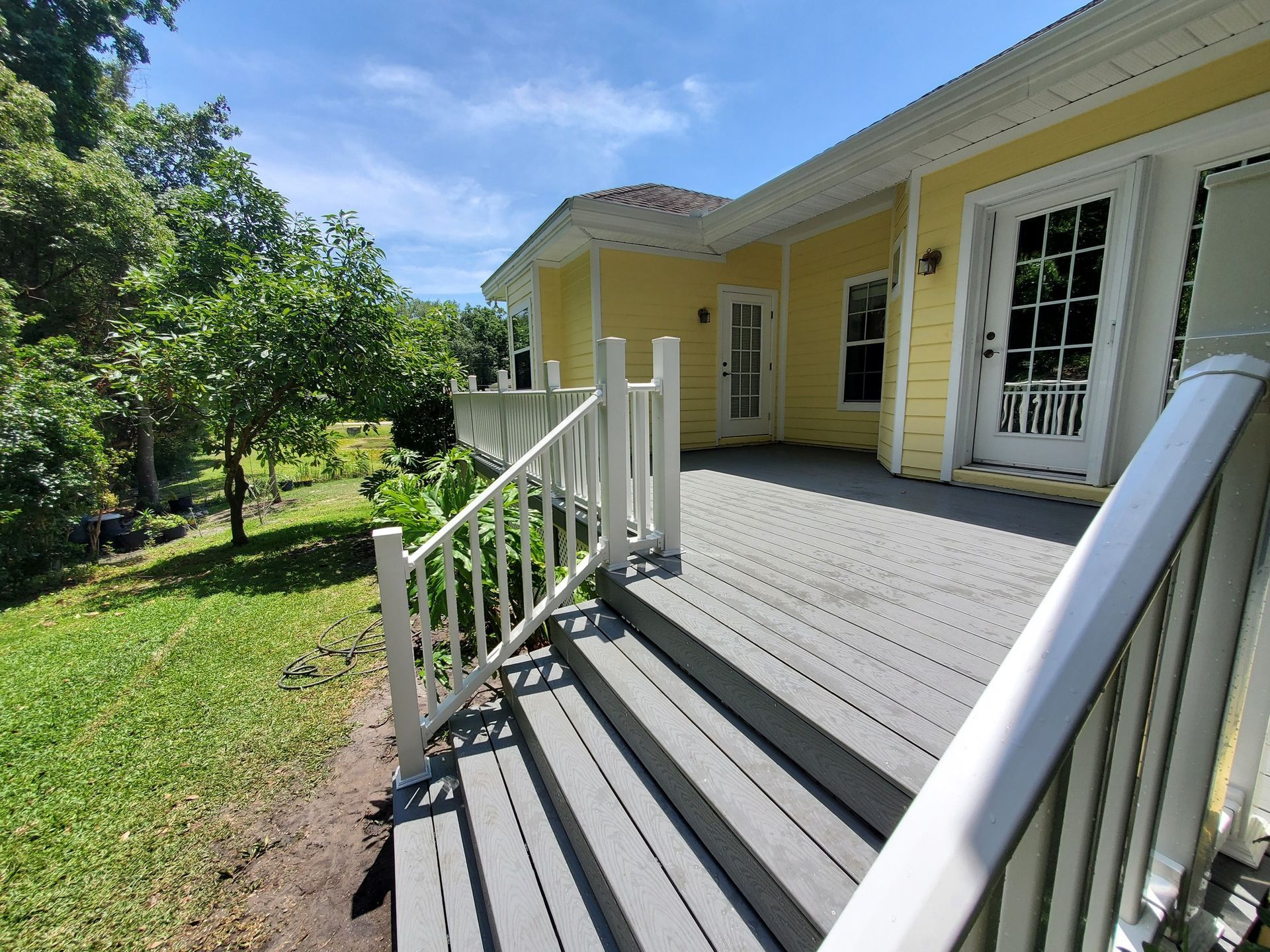 Yellow house with gray deck, white railing, and a door. Sunny outdoor scene.