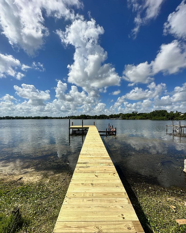Wooden pier extending into a calm lake under a partly cloudy blue sky.
