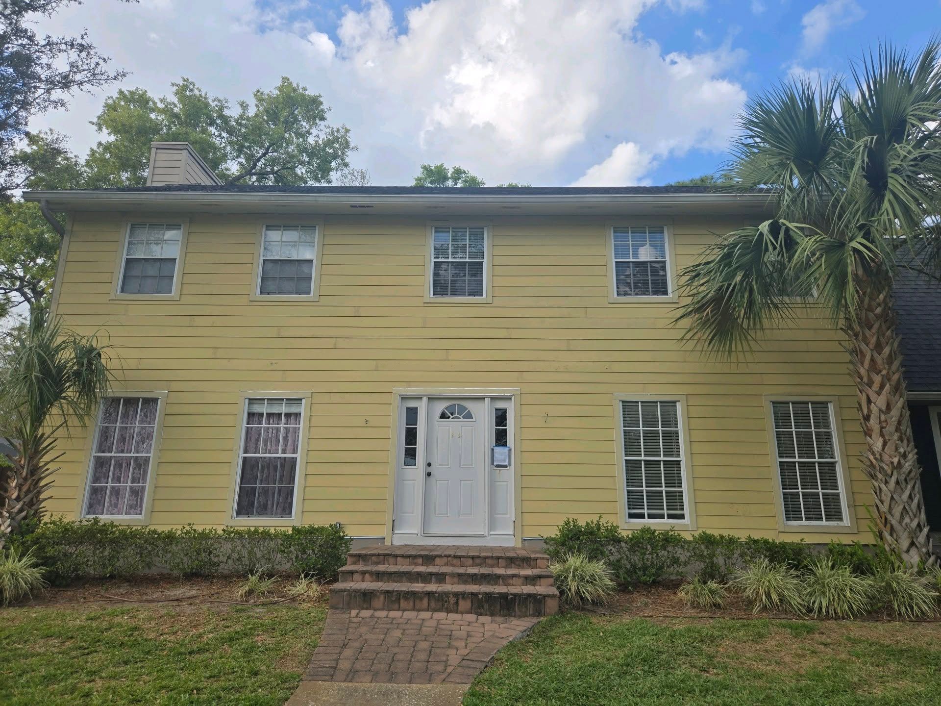 Yellow two-story house with white door and windows; palm trees flank the sides.