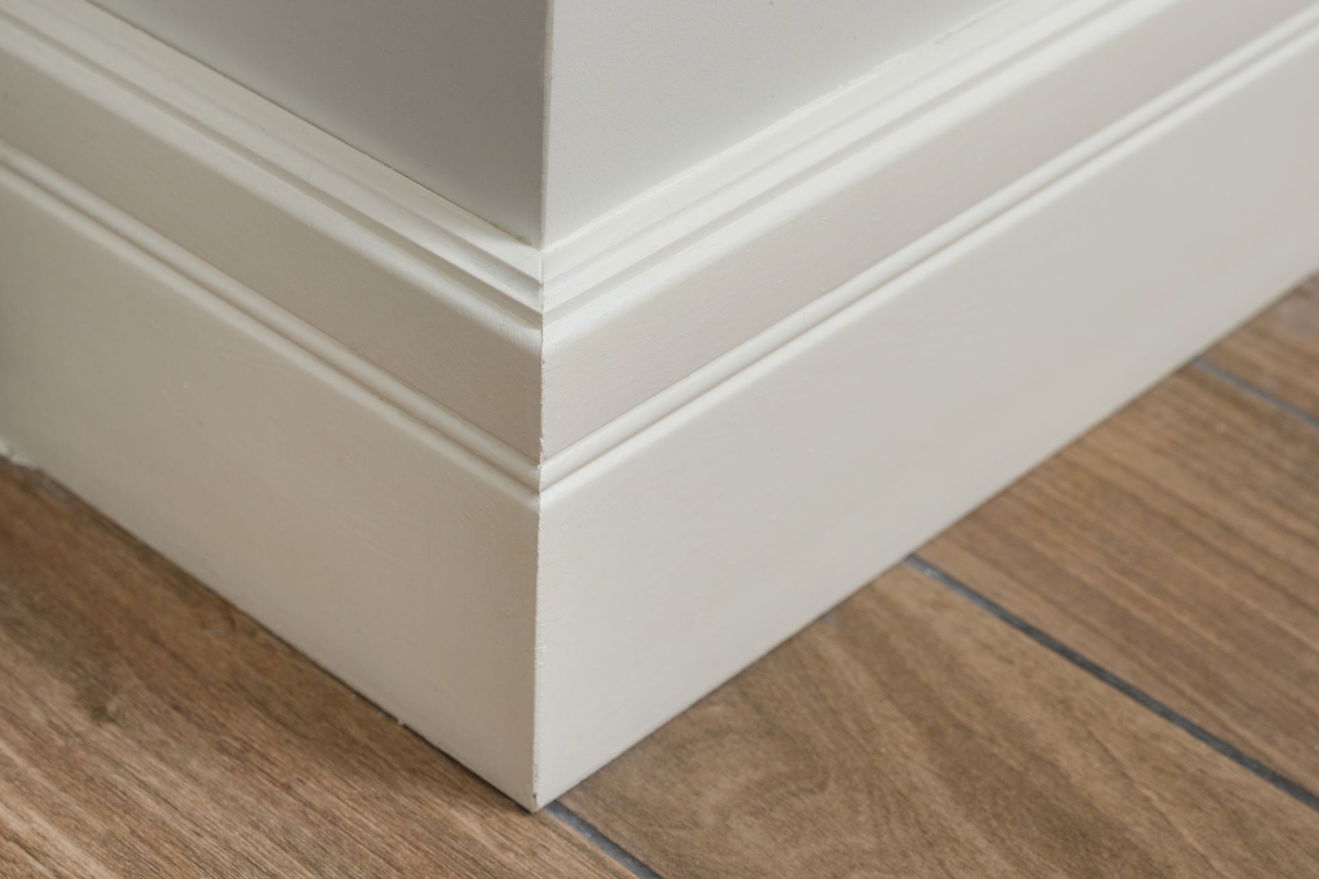 White-painted baseboard trim in a corner, with wood-look flooring.